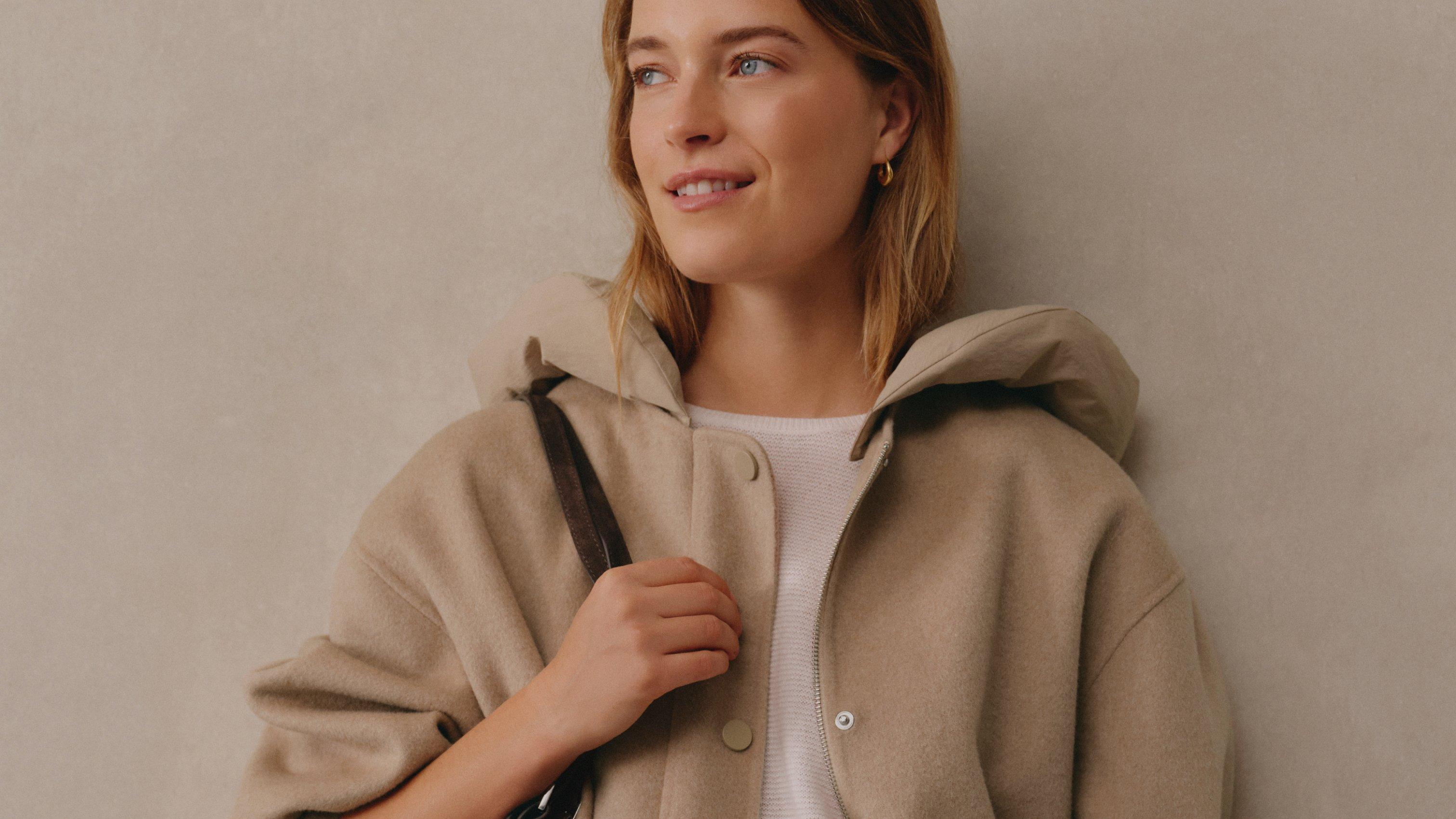 a woman in a beige jacket holding a purse against her shoulder